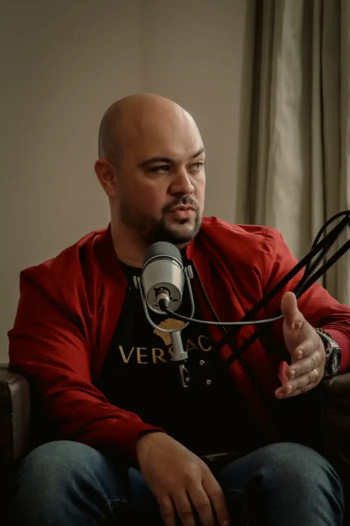 Alex Vilela de jaqueta vermelha, gravando um podcast